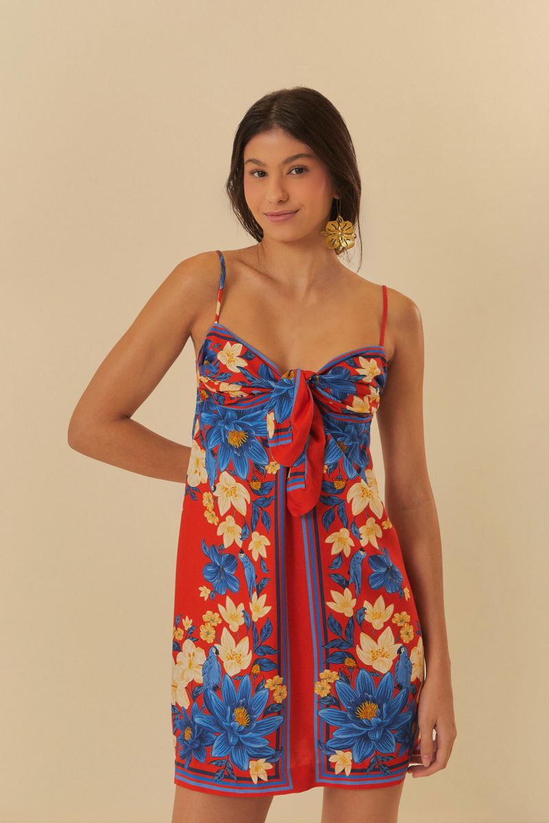 Imagen de un vestido corto con estampado floral vibrante en tonos de azul y rojo, con tiras delgadas y detalle de lazo al frente.