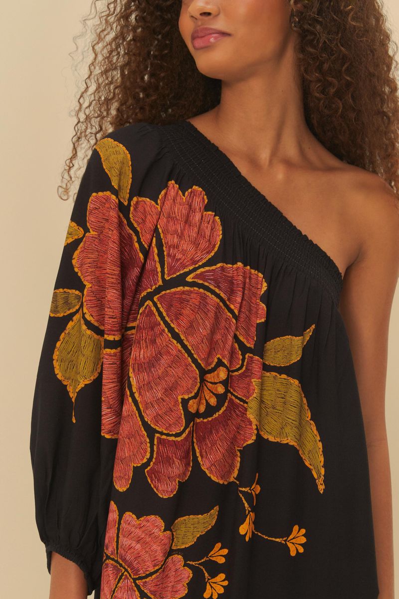 Detalle del escote del vestido negro con estampado floral, mostrando el acabado del único hombro.