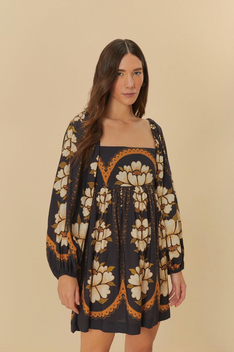 Modelo vistiendo vestido corto con estampado floral en tonos negro, blanco y naranja, con mangas largas abullonadas y escote cuadrado.