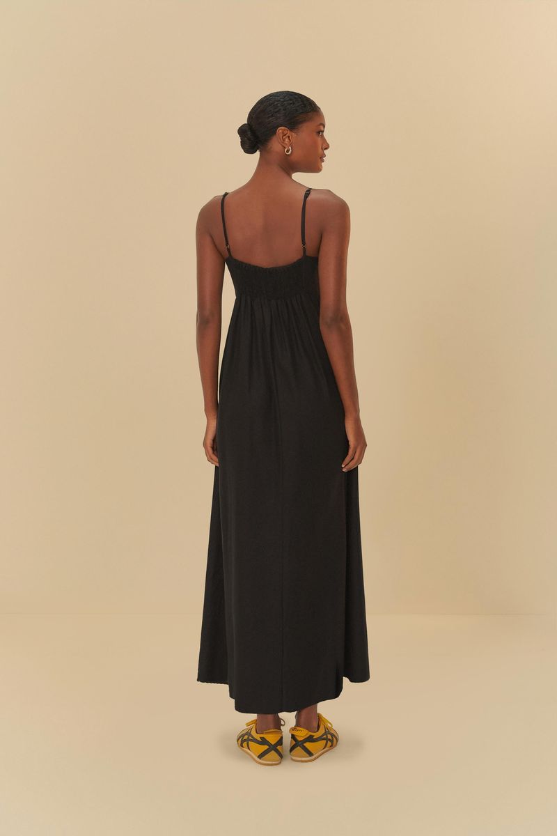 Vestido largo negro con tirantes finos, visto de espaldas, sobre fondo beige.