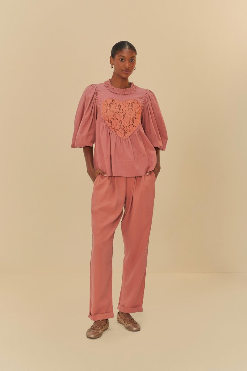 Imagen de una blusa rosada con detalles de encaje que forman un corazón en el centro, vista completa.