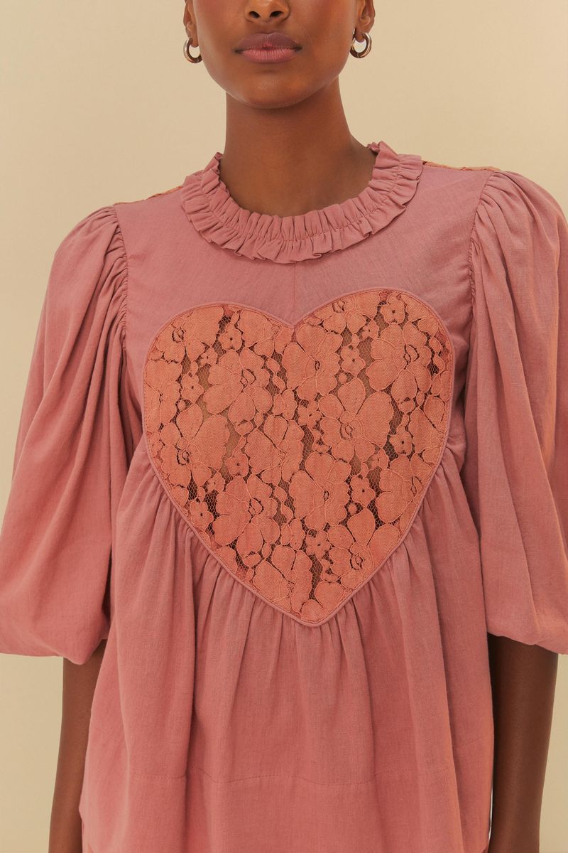Imagen de una blusa rosada con detalles de encaje que forman un corazón en el centro, vista detallada.