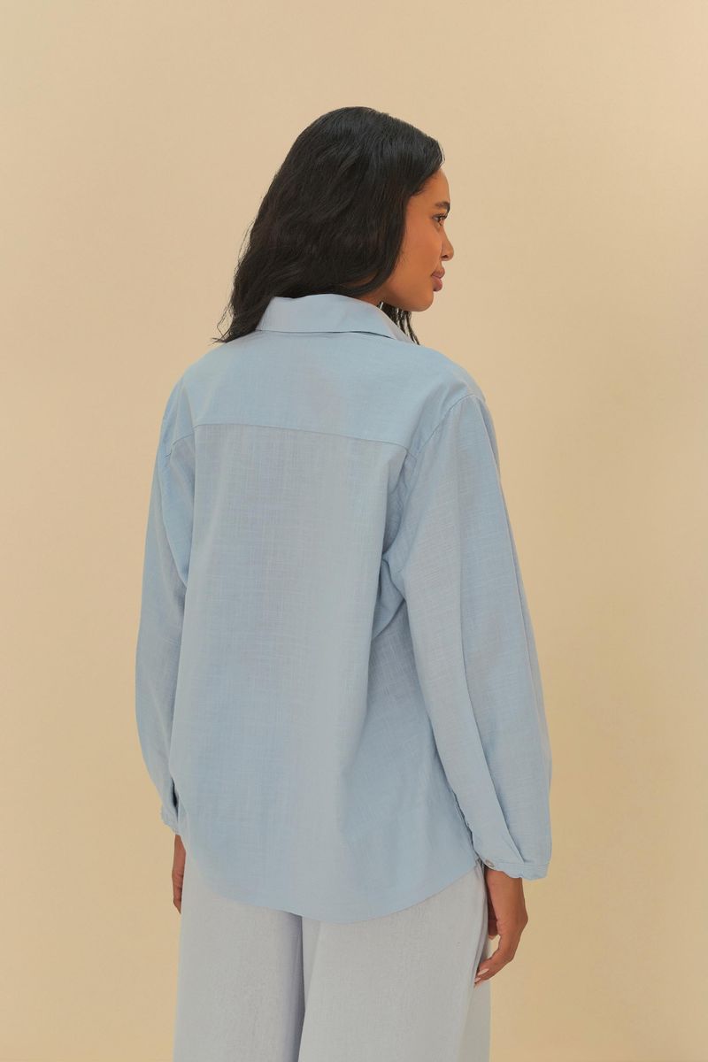 Vista trasera de la camisa azul clara con pliegues.
