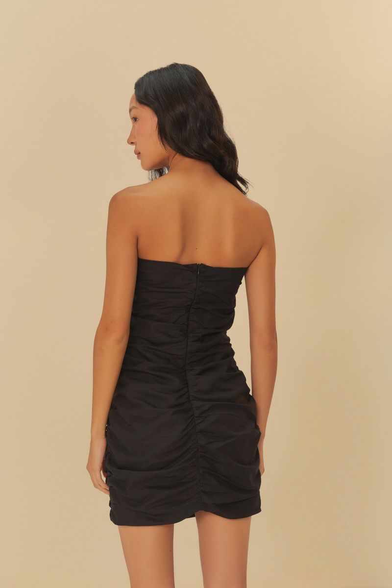 Vestido corto negro sin tirantes con fruncidos visto de espaldas, destacando el diseño ajustado y el acabado trasero.