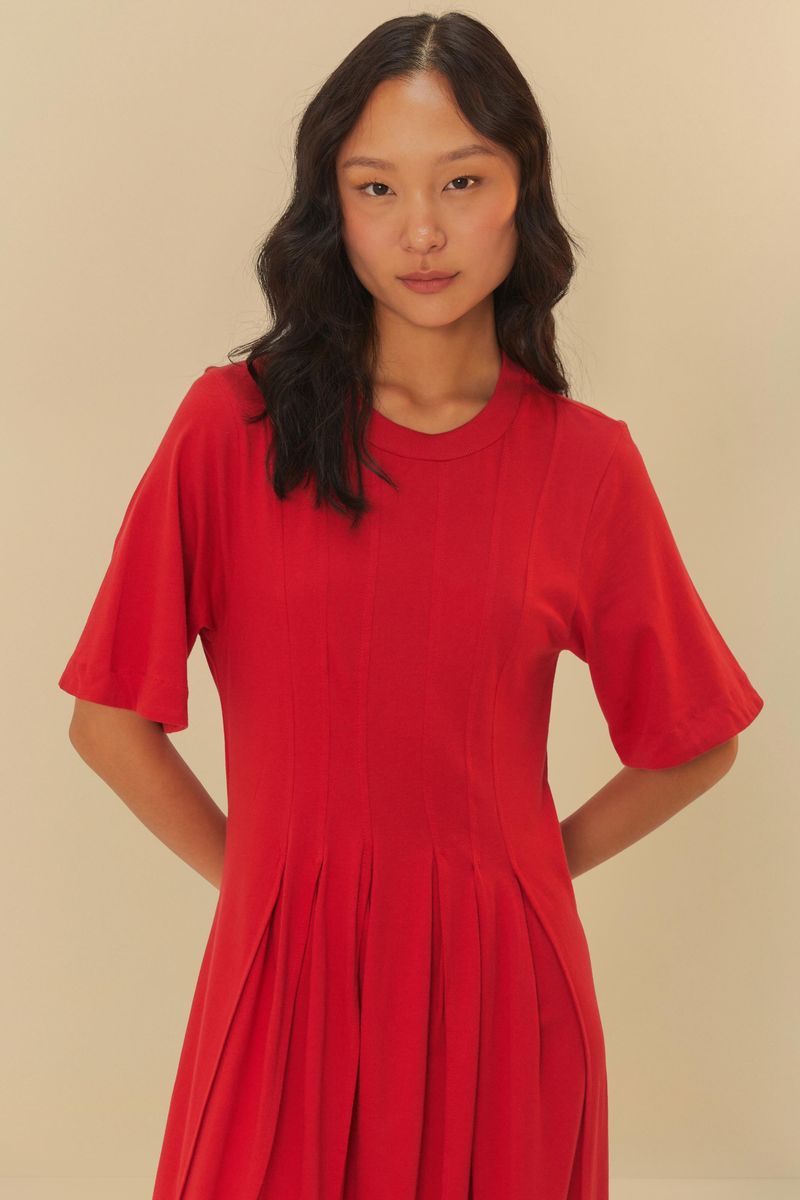 Imagen de una mujer usando un vestido corto rojo con pliegues, detalle del corpiño.