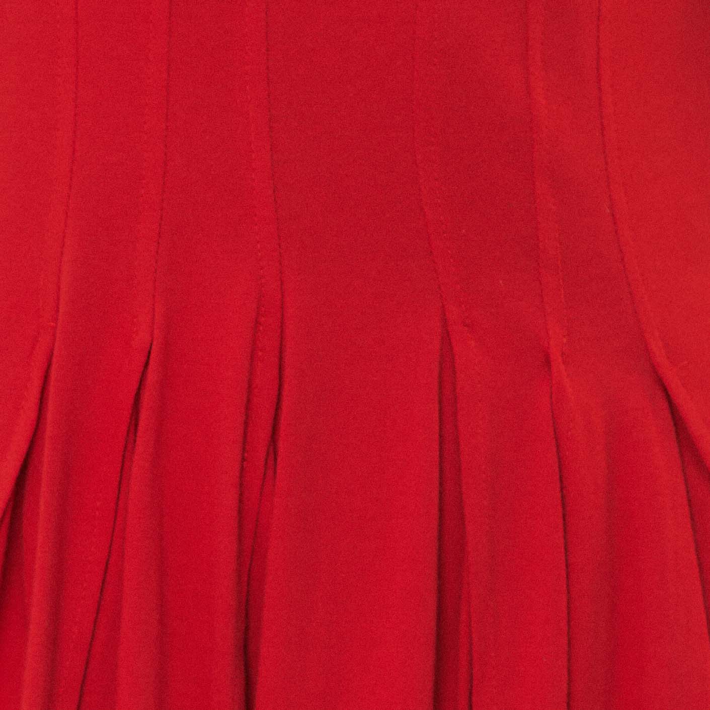 Imagen de una mujer usando un vestido corto rojo con pliegues, detalle del borde.
