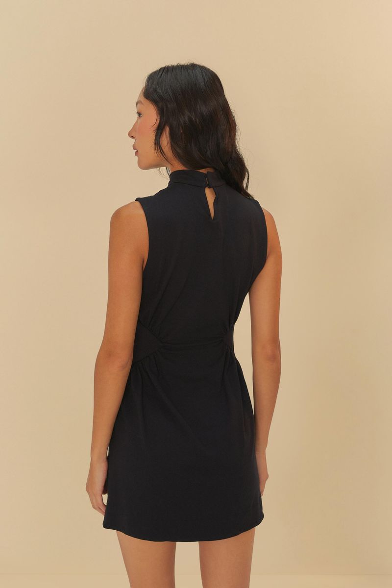 Imagen de un vestido negro con cuello alto y detalle torcido en la cintura, visto de espaldas.