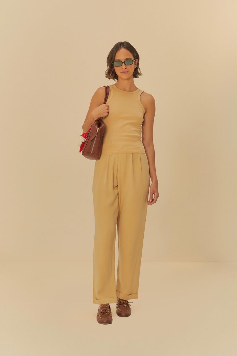 Imagen de una camiseta sin mangas beige en un conjunto completo con pantalón beige y accesorios.