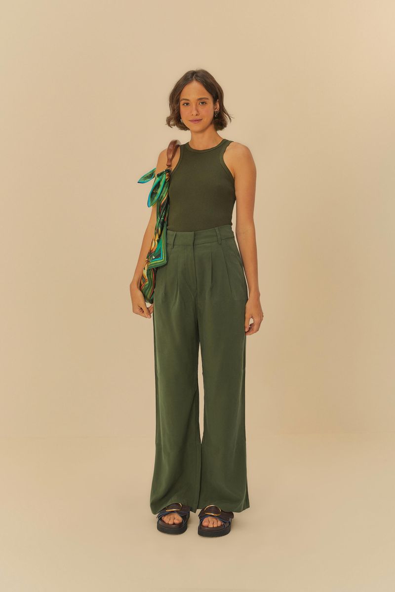 Modelo de pie vistiendo regata verde oscuro y pantalón verde, sosteniendo un bolso.