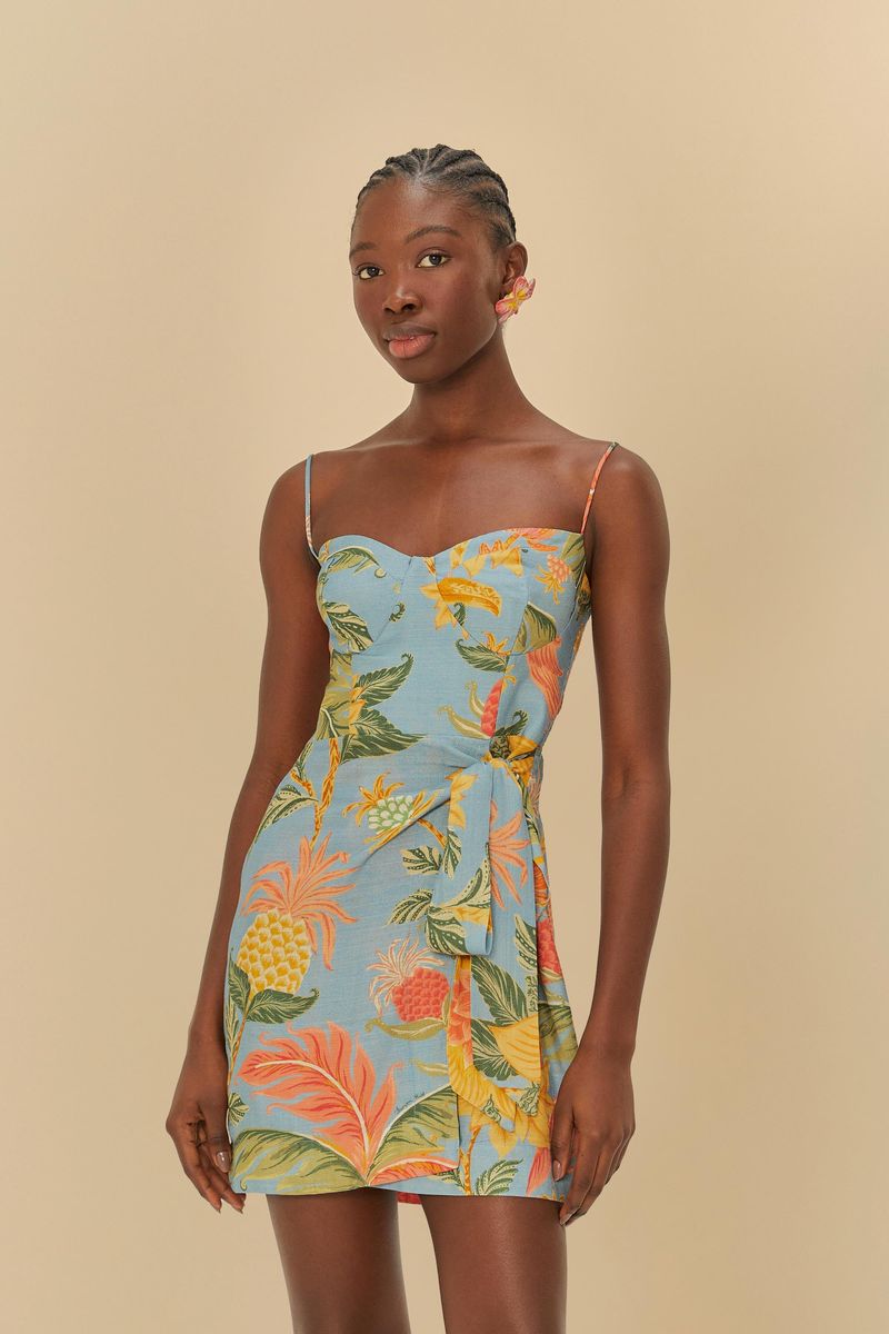 Vestido cruzado con estampado tropical en fondo azul, tirantes delgados y largo corto, visto de frente.