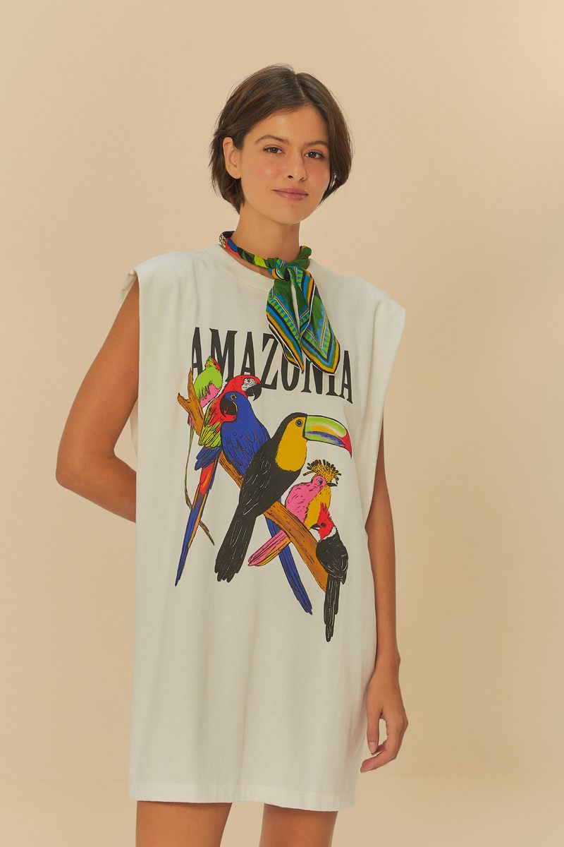 Modelo usando un vestido corto blanco con estampado de pájaros coloridos y el texto 'Amazonia', vista frontal.