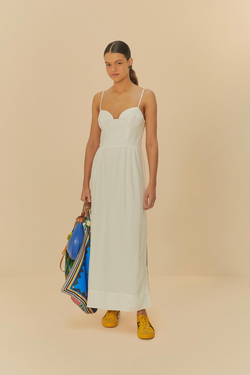 Modelo usando vestido largo blanco con escote redondo y tirantes, sosteniendo una bolsa azul y luciendo zapatos amarillos.