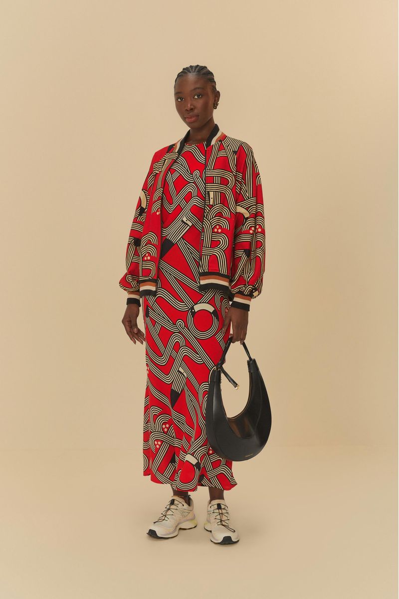 Modelo que lleva un vestido largo estampado con patrón geométrico en rojo y negro, combinado con una chaqueta estampada y zapatillas blancas.