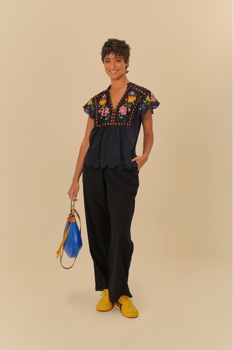 Modelo vistiendo pantalón negro de sastrería con pinzas, combinado con blusa bordada y accesorios coloridos.
