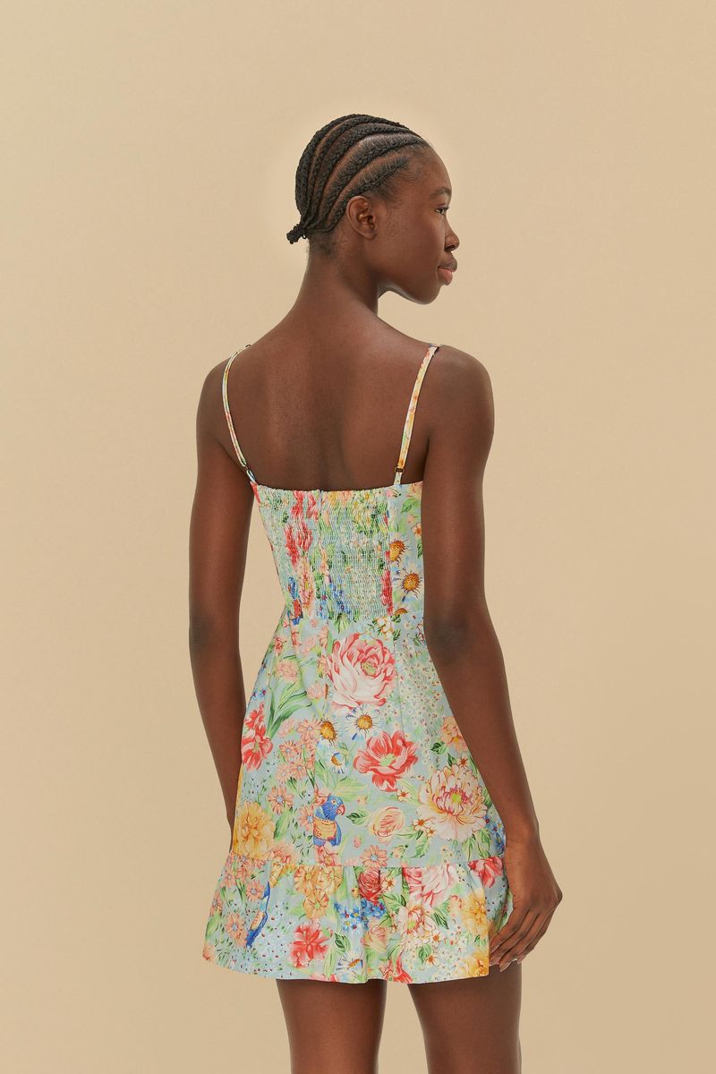 Vista trasera del vestido corto con estampado floral y de pájaros, tirantes finos y detalle de la basta.