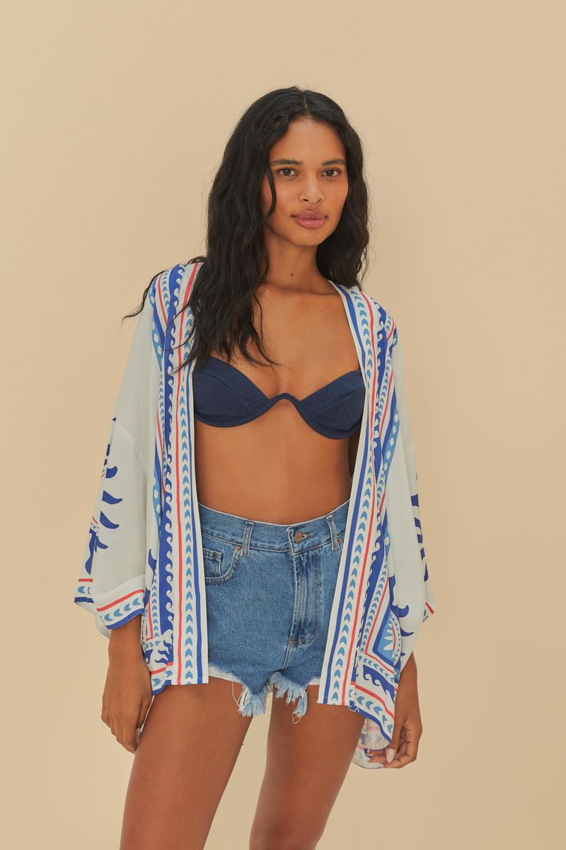 Modelo usando shorts de mezclilla curvo desgastado con cintura alta y terminación deshilachada, combinado con un top azul y un kimono estampado.