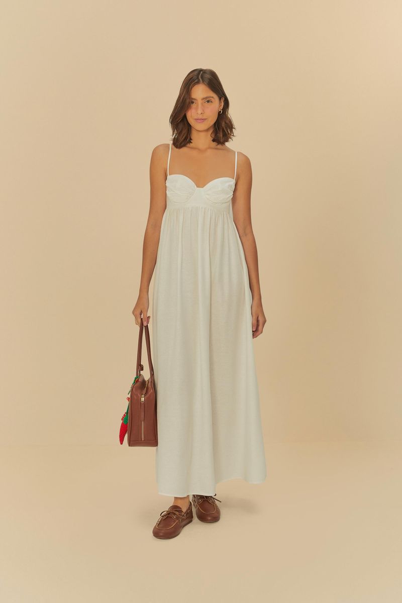Imagen de una mujer usando un vestido largo fruncido blanco con tirantes delgados, llevando un bolso marrón y usando sandalias marrones.