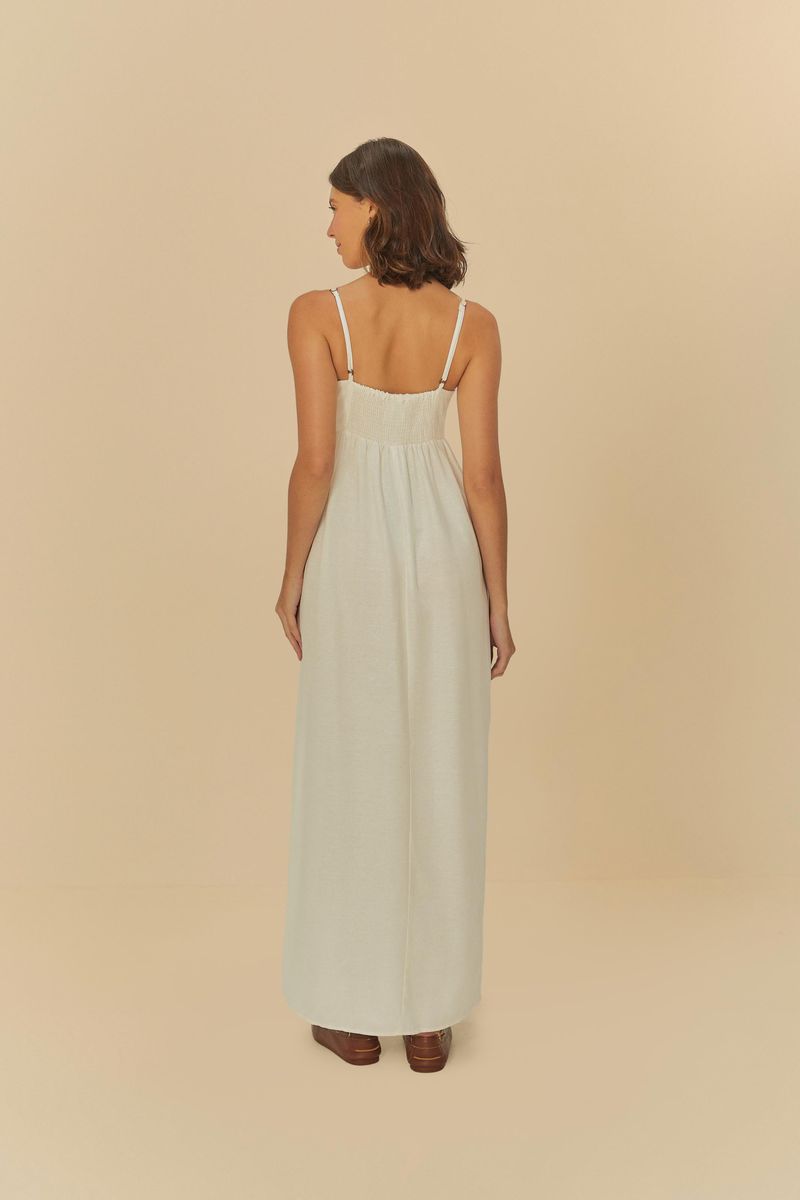 Imagen trasera de una mujer usando un vestido largo fruncido blanco con tirantes delgados.