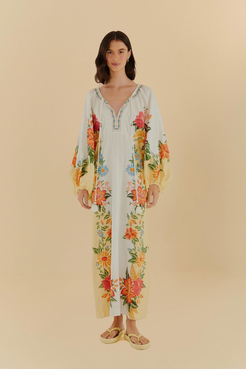 Vestido largo floral con mangas largas y estampado tropical sobre fondo beige, visto de frente.
