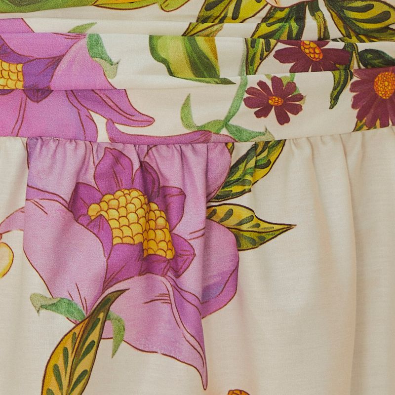 Vestido largo estampado con tirantes finos, fondo beige y flores coloridas, visto desde atrás.