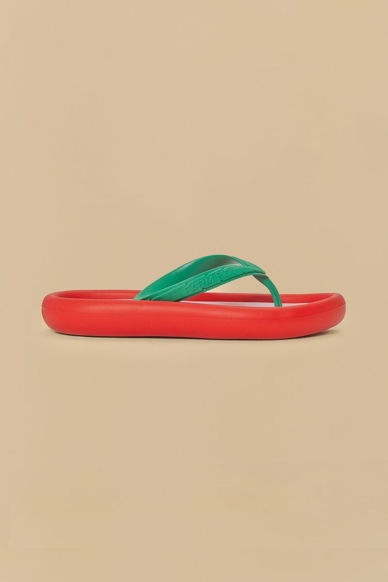 Imagen de un chinelo rojo con tiras verdes sobre fondo beige.