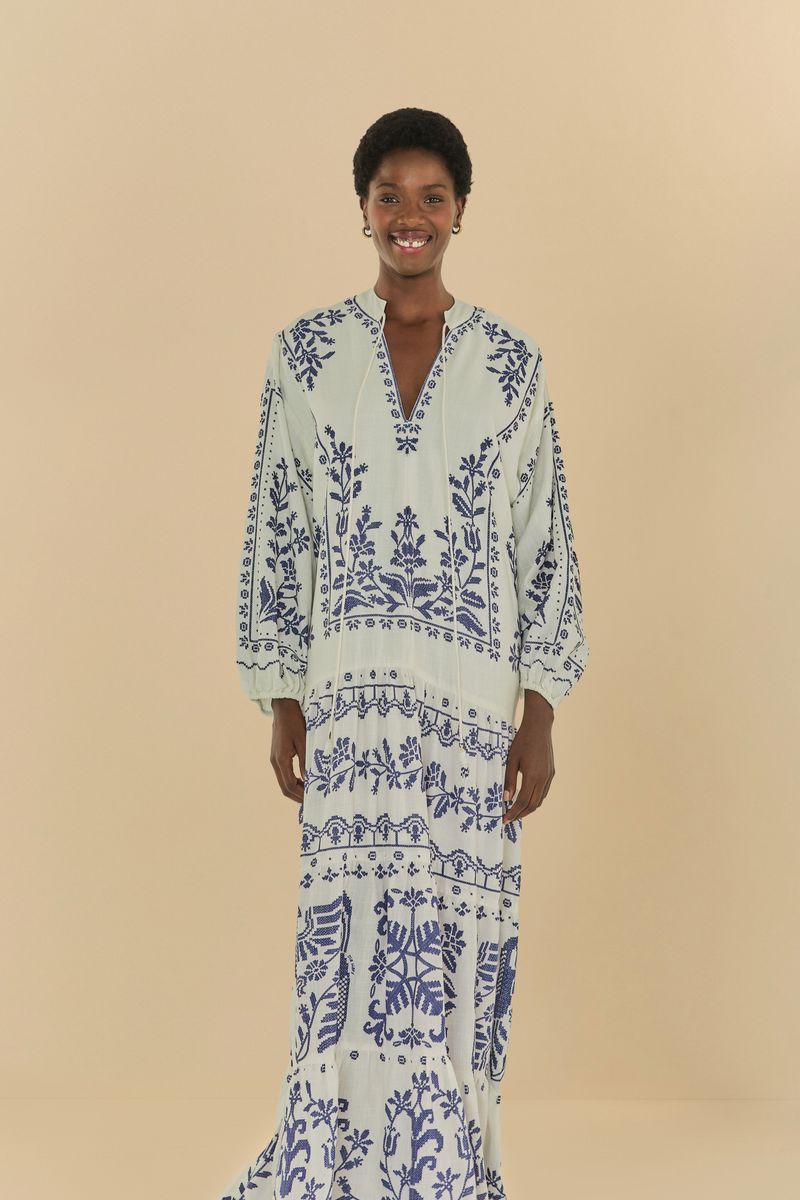 Vestido largo con bordado tropical azul sobre fondo claro, vista frontal superior.