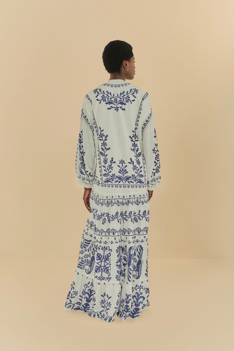 Vestido largo con bordado tropical azul sobre fondo claro, vista trasera completa.