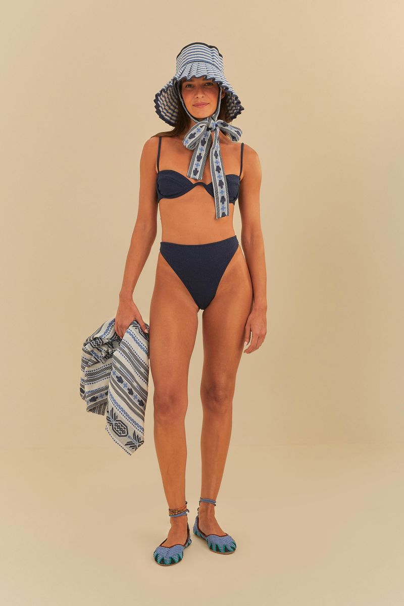 Modelo usando un bikini azul con textura de palma, sombrero de playa y bolso geométrico.