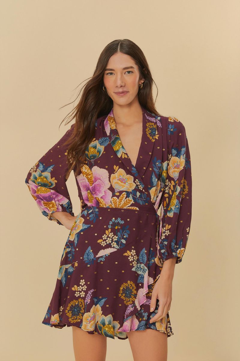 Imagen de una mujer usando un vestido corto estampado con flores sobre un fondo morado, vista frontal.