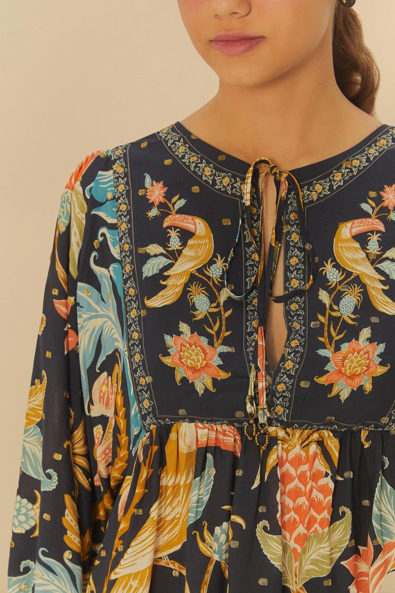 Detalle del escote en V con amarre y estampado floral y de pájaros, fondo beige.