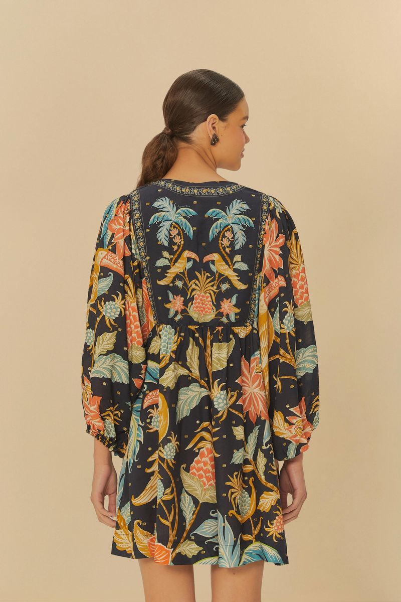 Vista trasera del vestido corto estampado con mangas largas y patrón floral y de pájaros, fondo beige.