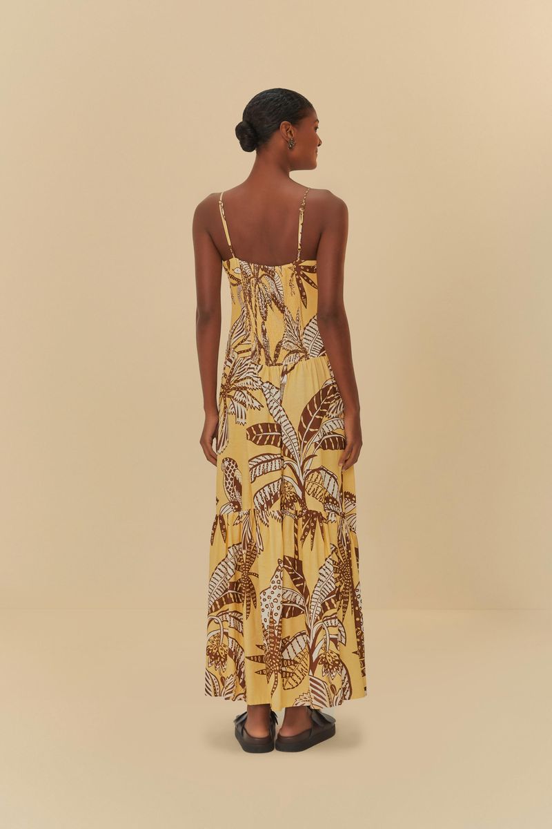 Imagen lateral de un vestido largo con tirantes finos, estampado con motivos botánicos en tonos de amarillo y marrón, mostrando la caída de la tela.