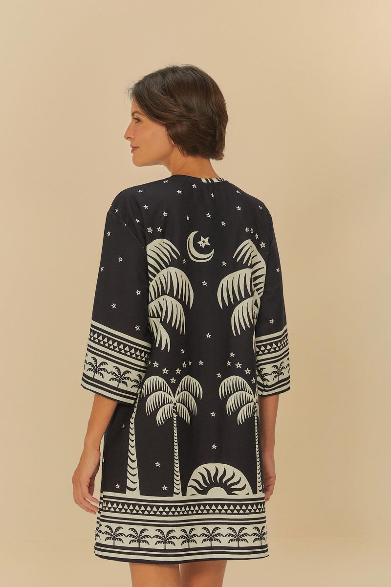 Vista trasera del vestido con estampado de palmeras y elementos celestiales sobre fondo oscuro.