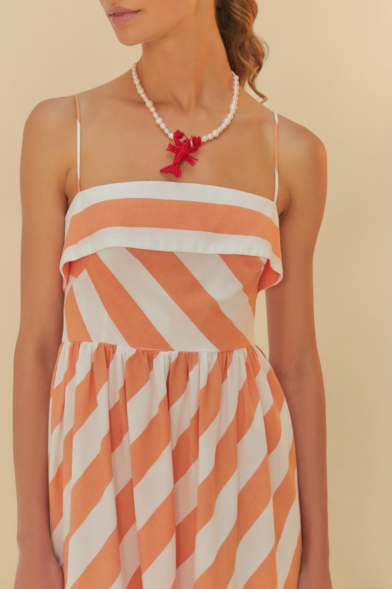 Detalle del escote del vestido con tirantes finos y estampado de rayas diagonales en tonos de naranja y blanco.