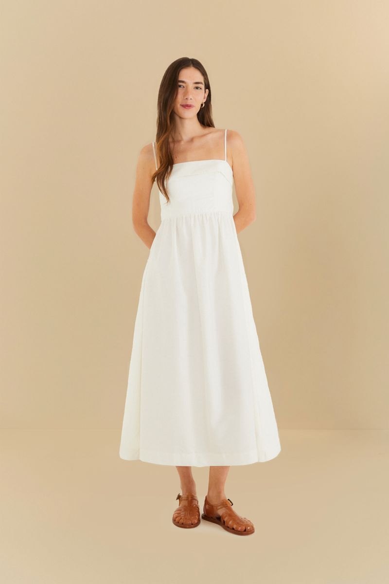 Imagen de un vestido largo blanco con tirantes delgados, presentado sobre un fondo beige.
