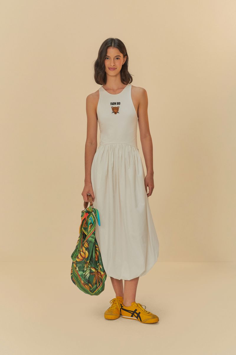 La modelo lleva un vestido blanco con bordado de tigre en la parte superior, sosteniendo una bolsa estampada y calzando zapatos amarillos.