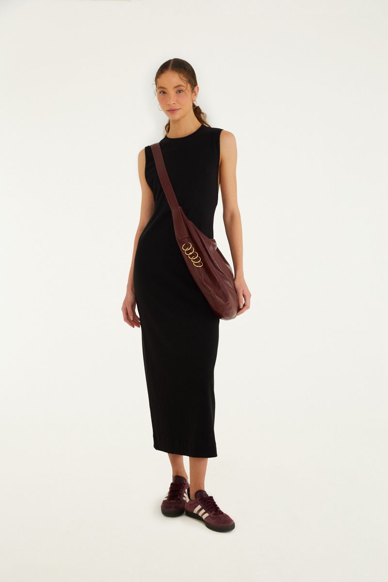 Imagen de una modelo vistiendo un vestido negro con escote redondo y largo midi, complementado con tenis casuales y un bolso cruzado.