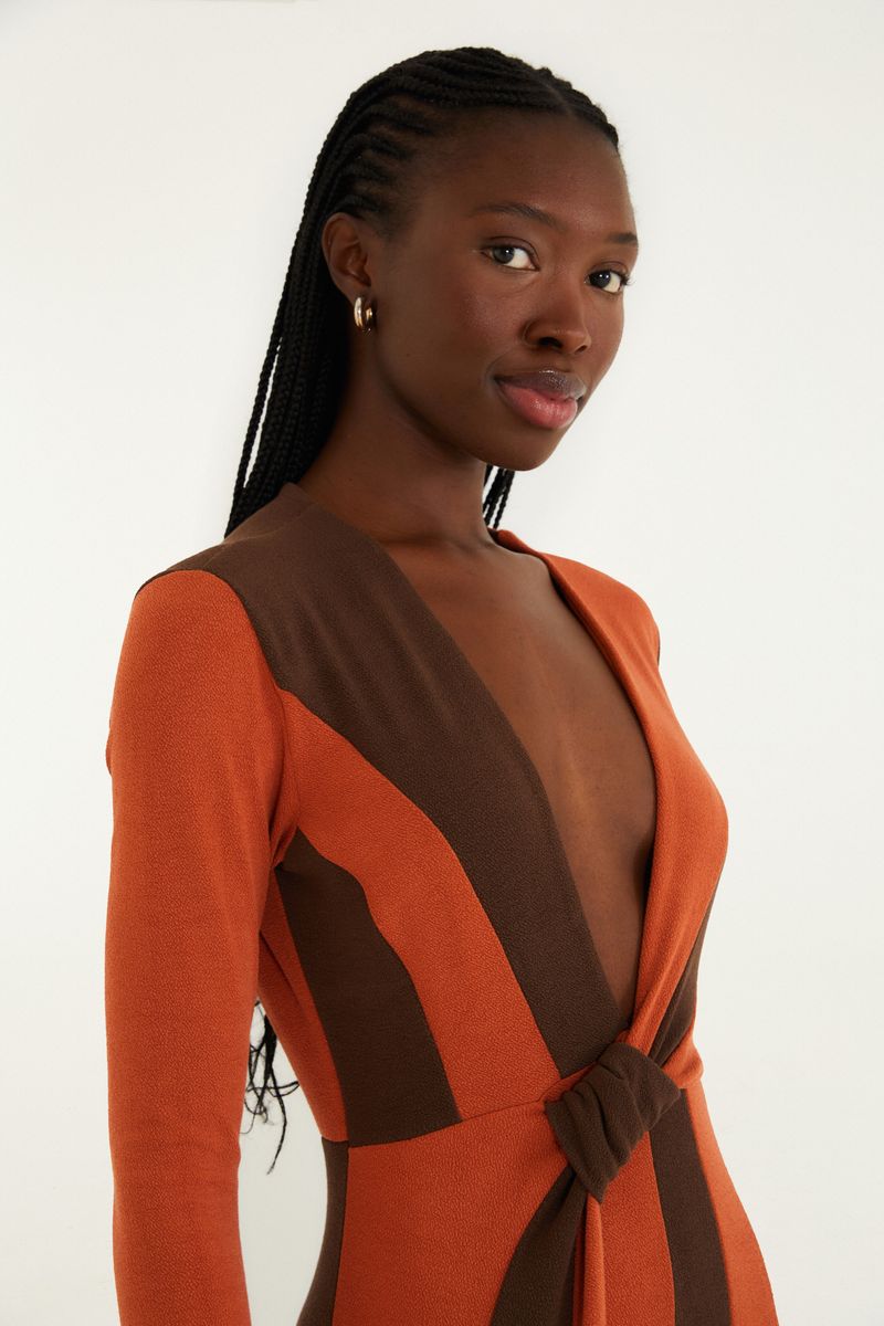 Detalle del escote profundo en V del vestido largo con estampado geométrico en tonos de marrón y naranja.