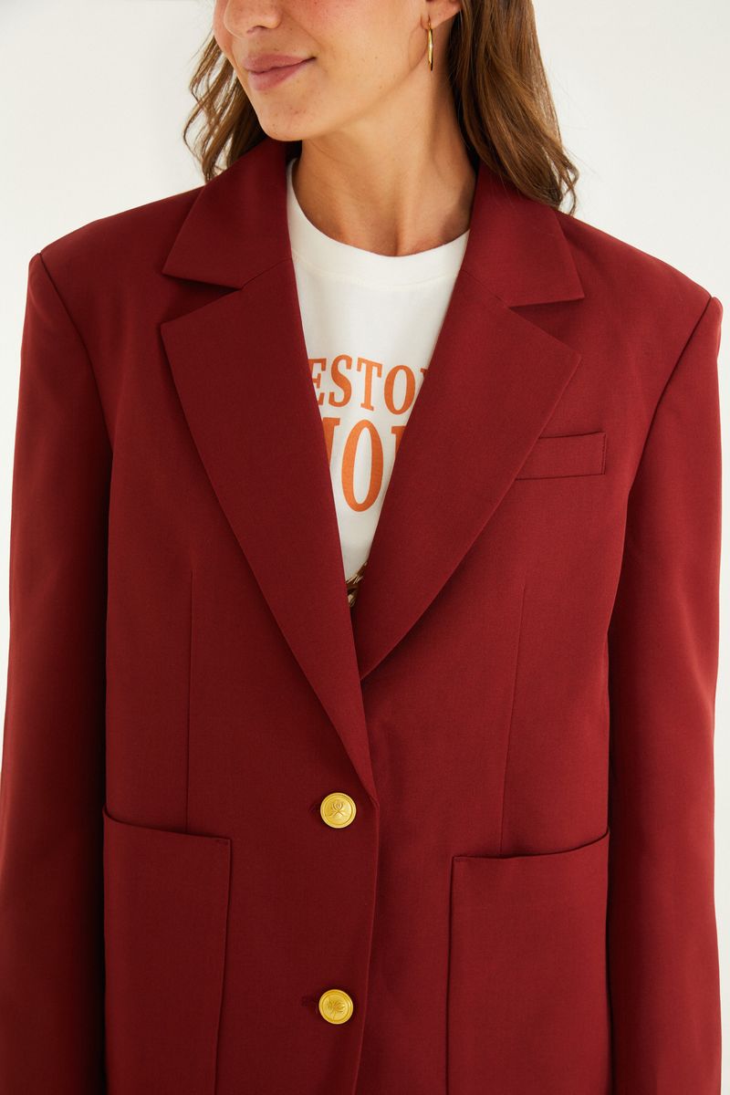 Detalle de la solapa y cierre del blazer rojo con botones dorados.