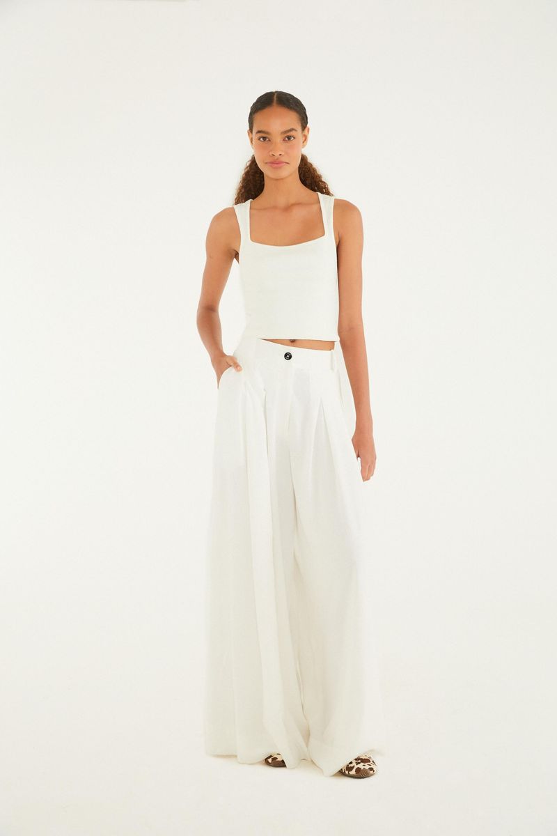 Imagen de una camiseta de tirantes estilo cropped blanca vista de cuerpo entero, mostrando su combinación con pantalones amplios.