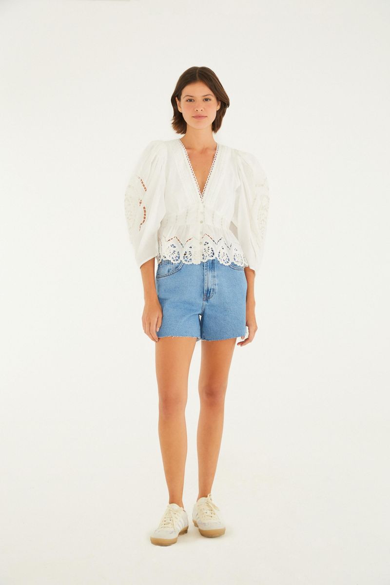 Modelo usando un short jean azul con cintura alta y blusa blanca.