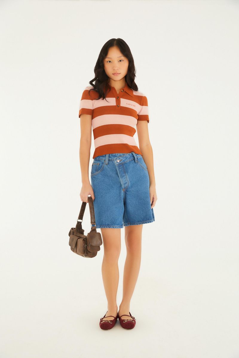 Modelo vistiendo camisa polo de tejido tricot con rayas horizontales en tonos marrón y rosa, combinada con pantalones cortos de denim.
