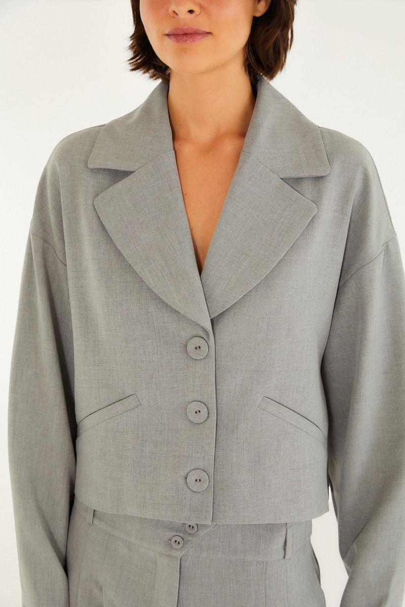Detalle del blazer de alta costura en mezcla gris con solapa entallada y cierre de botones.