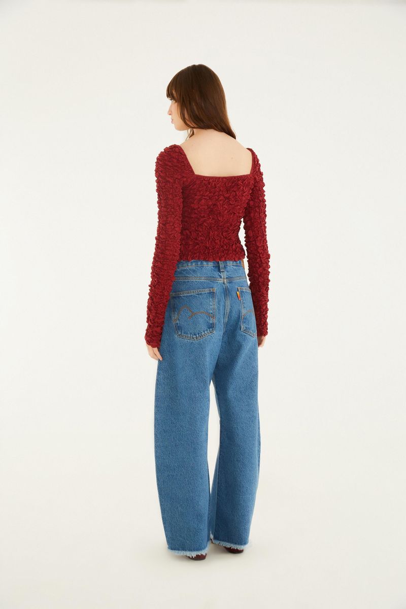 Vista trasera del jean suelto con blusa texturizada roja.