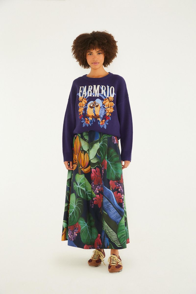Modelo vistiendo falda larga estampada con elementos tropicales y fondo azul oscuro, vista frontal.