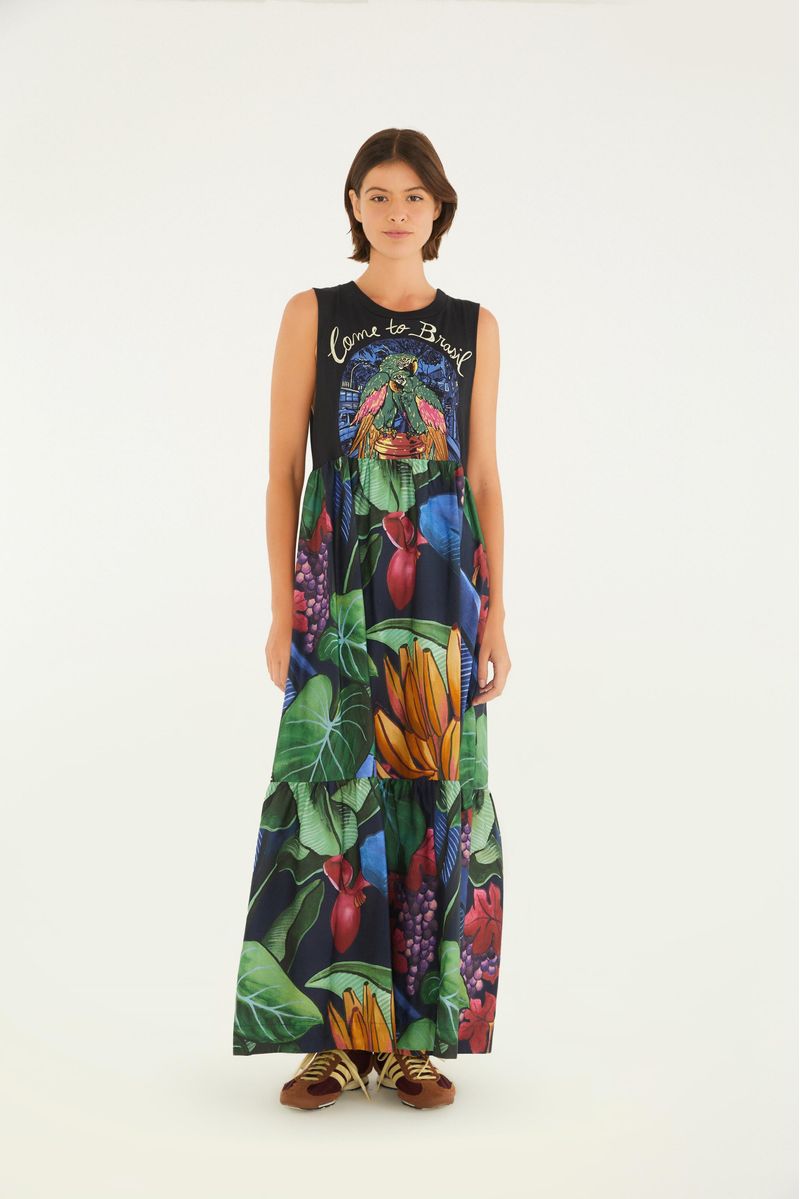 Imagen de una mujer vistiendo un vestido largo estampado de tema tropical, con detalles de hojas y frutas, vista frontal.
