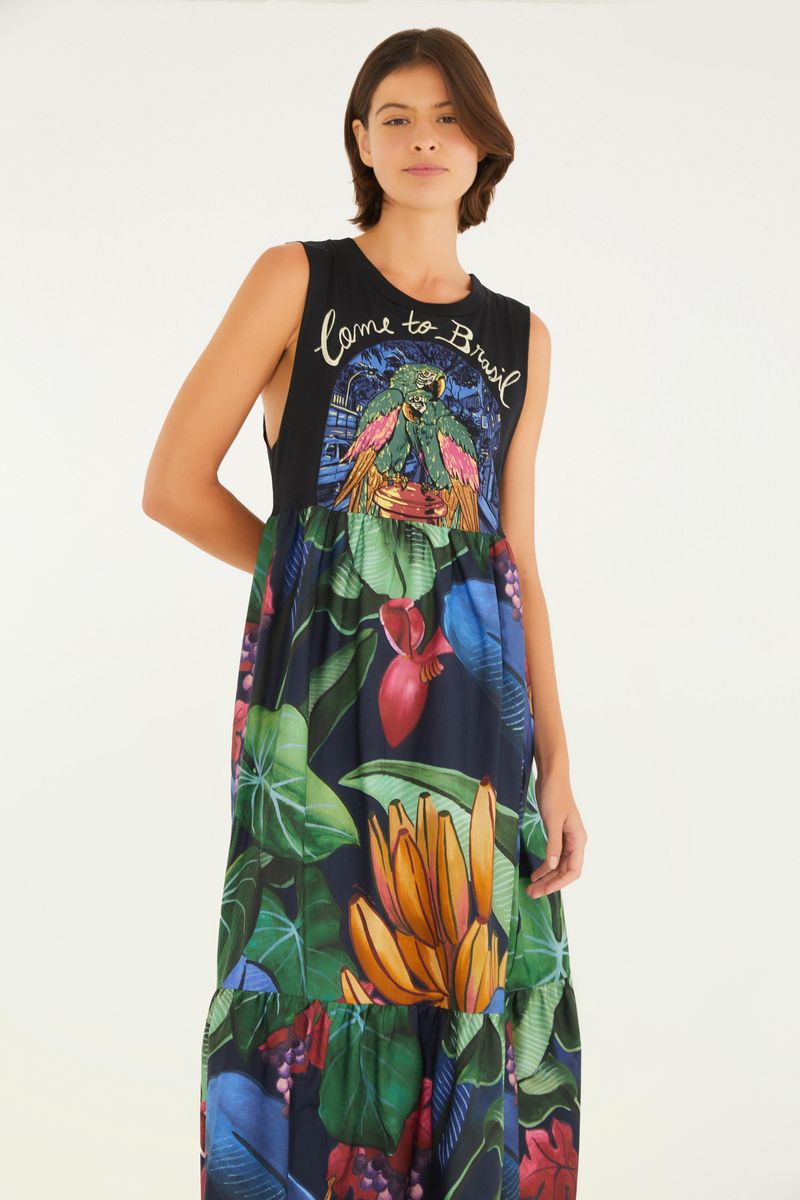 Imagen de una mujer vistiendo un vestido largo estampado de tema tropical, con detalles de hojas y frutas, vista trasera.