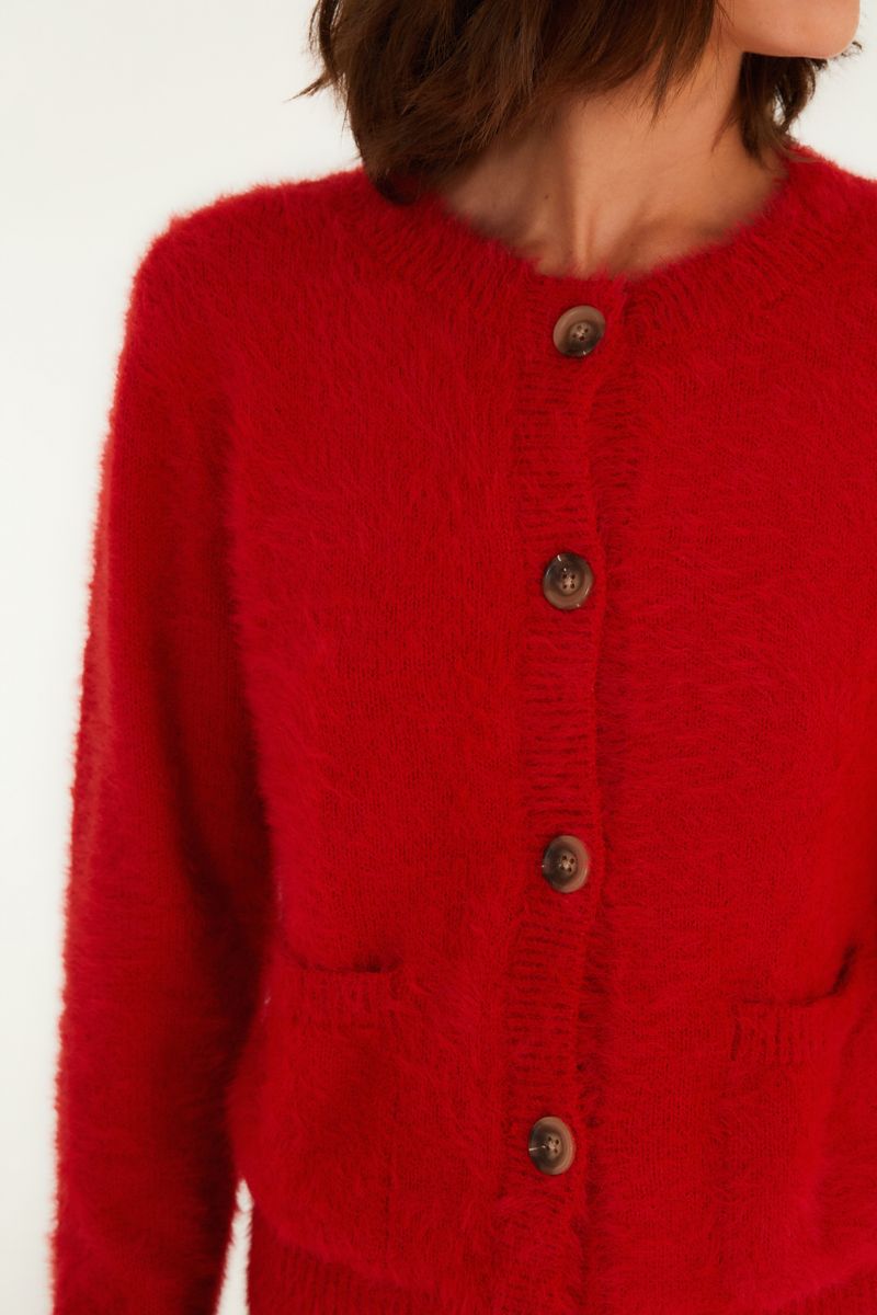 Detalle del cardigan rojo que muestra los botones y bolsillos frontales.