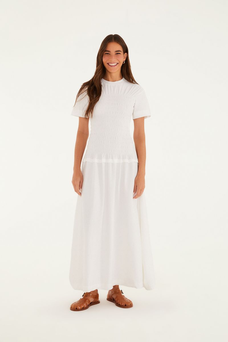 Vestido blanco estilo camiseta con abertura lateral, largo completo, presentado en modelo.