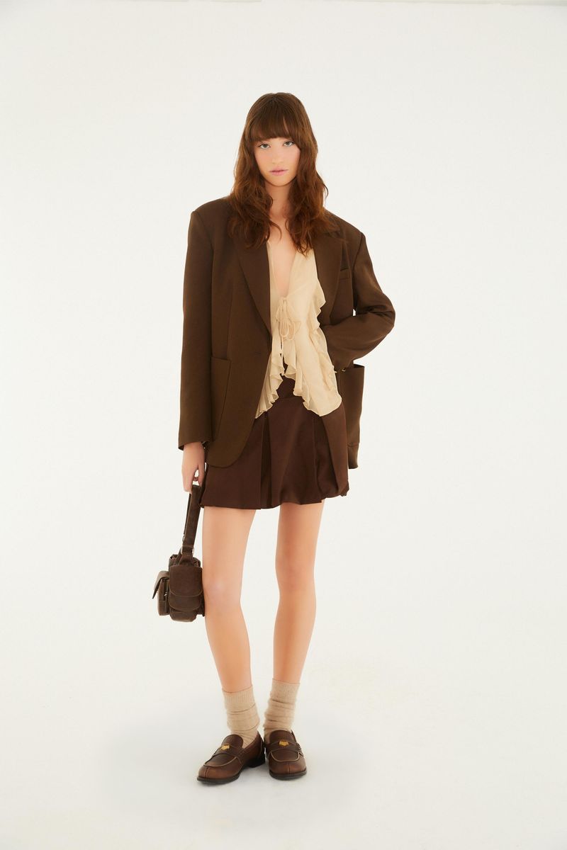 Modelo usando la falda Balone Pregas marrón con blazer y zapatos, mostrando un conjunto completo.